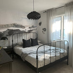 A watercolor wall mural named "Atmospheric Abstraction" featured in a modern bedroom setting. The mural's abstract design in soft greys and whites creates a tranquil atmosphere, complemented by a metal bed frame, gray bedding, and minimalist decor, enhancing the room's contemporary aesthetic.
