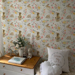 A charming child's room adorned with Garden Bunnies Wallpaper showcasing adorable rabbits and colorful flowers. The decor includes a white dresser topped with plush toys and children's books, enhancing the room's whimsical feel.