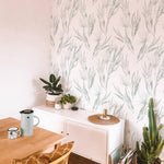 A stylish home office setup featuring the White Watercolour Floral Wallpaper V - Light Sage on one wall, paired with a modern white sideboard, various indoor plants, and minimalist decor