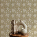 Artistic display against a mustard-colored Cornflower Wallpaper, showcasing an intricate design of beige and off-white floral motifs. The composition includes two unique ceramic vases on a rustic wooden stool, enhancing the vintage aesthetic of the space.