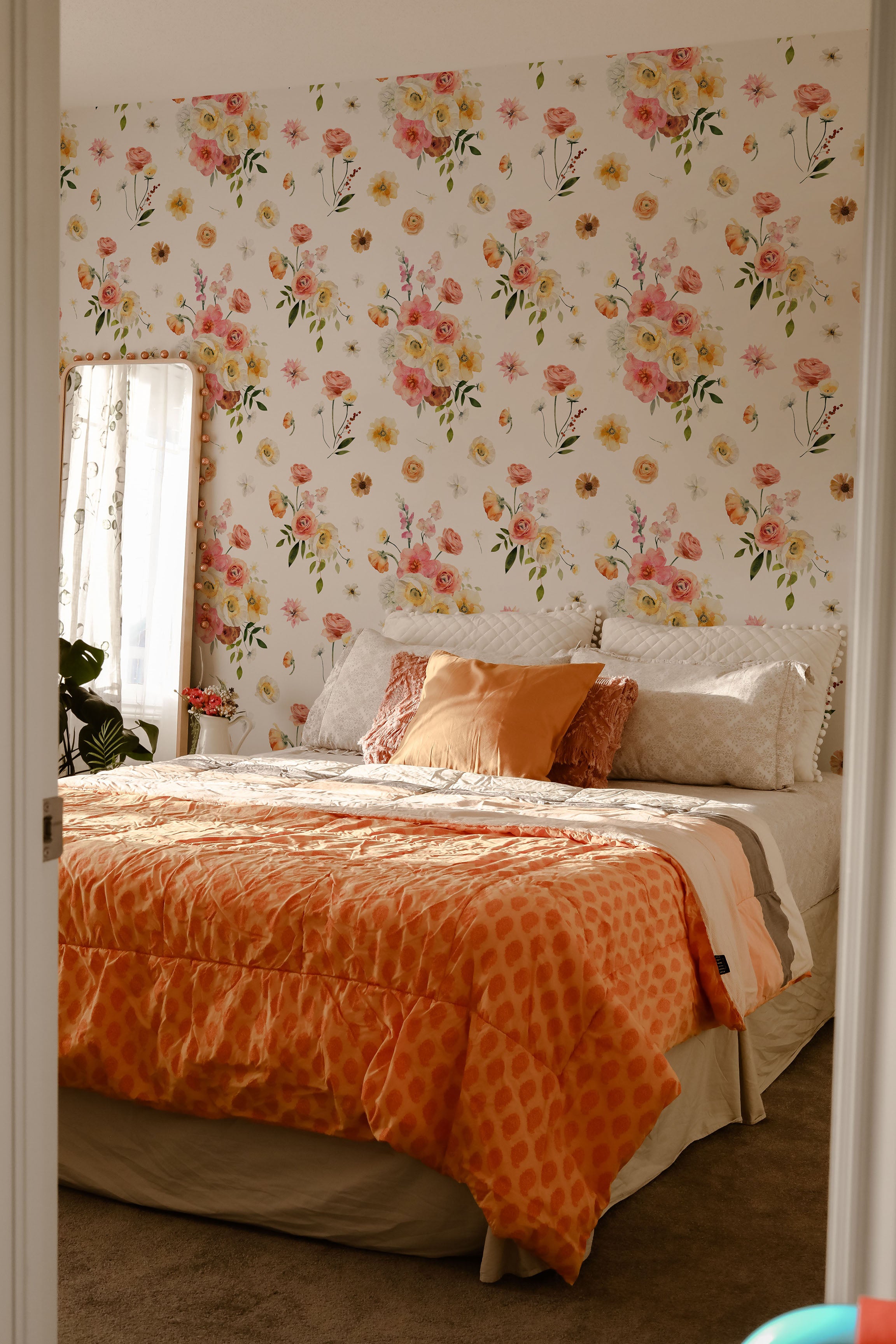 Golden Garden Wallpaper showcasing a lively floral design in a bedroom, with a neatly made bed adorned with orange bedding and pillows, and sunlight streaming through the window