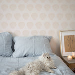 A fluffy white cat lounging on a bed covered with light blue linens against a backdrop of Mermaid Sea Shell wallpaper. The soft pink shells on the wallpaper add a tranquil and decorative element to the room