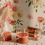 Golden Garden Wallpaper featuring a detailed floral design, with a decorative arrangement including a pink candle and a vase placed against the wallpaper.