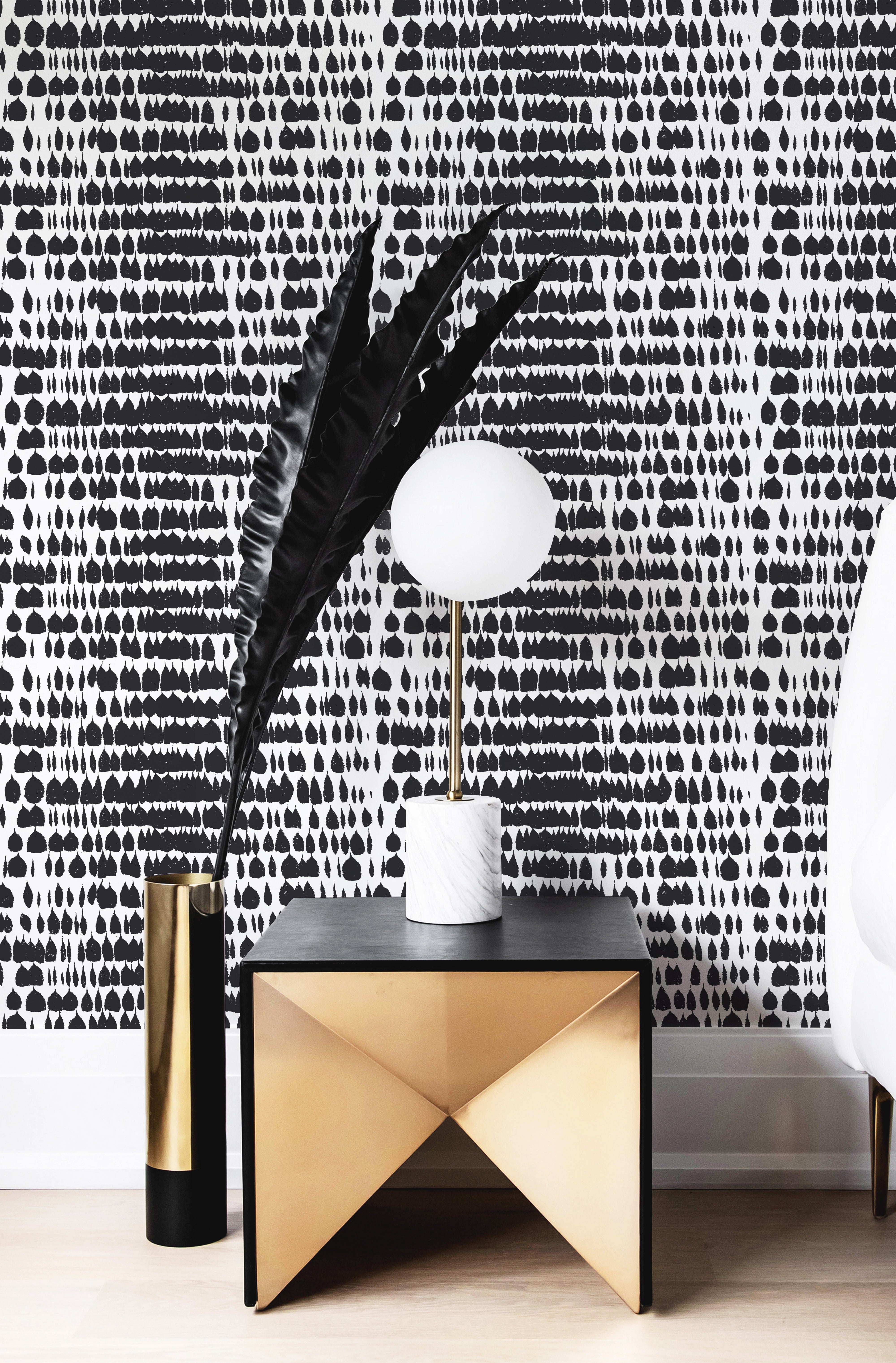 An elegant setting with the Bold Brilliance Wallpaper in a stylish room, complemented by a geometric black and gold table and a modern lamp with a white globe shade. The wallpaper adds a bold and artistic touch, enhancing the sophisticated ambiance of the room.