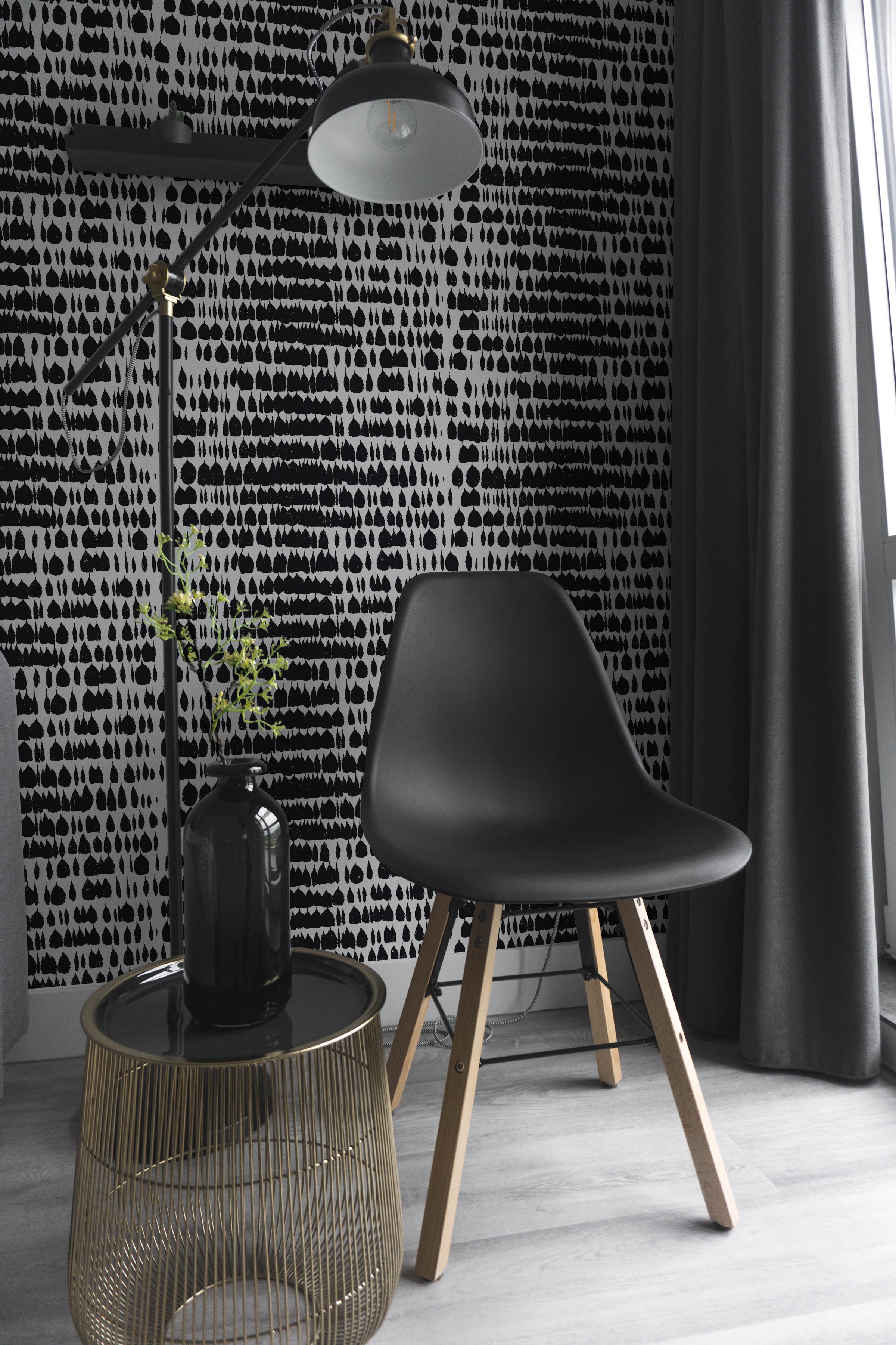 A modern interior featuring the Bold Brilliance Wallpaper with a distinctive black and white pattern that resembles inkblots or abstract brush strokes. The wallpaper creates a dynamic backdrop for a sleek black chair and a stylish floor lamp, accentuating a contemporary, minimalist decor.