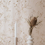 An elegant and sophisticated interior decor featuring Gold Leaves Wallpaper with hand-painted gold foliage patterns on a creamy background, complemented by a chic ceramic vase and candle holder.