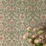 A close-up of a vase holding a variety of pale pink flowers, with the detailed pattern of the pastel floral damask wallpaper filling the frame