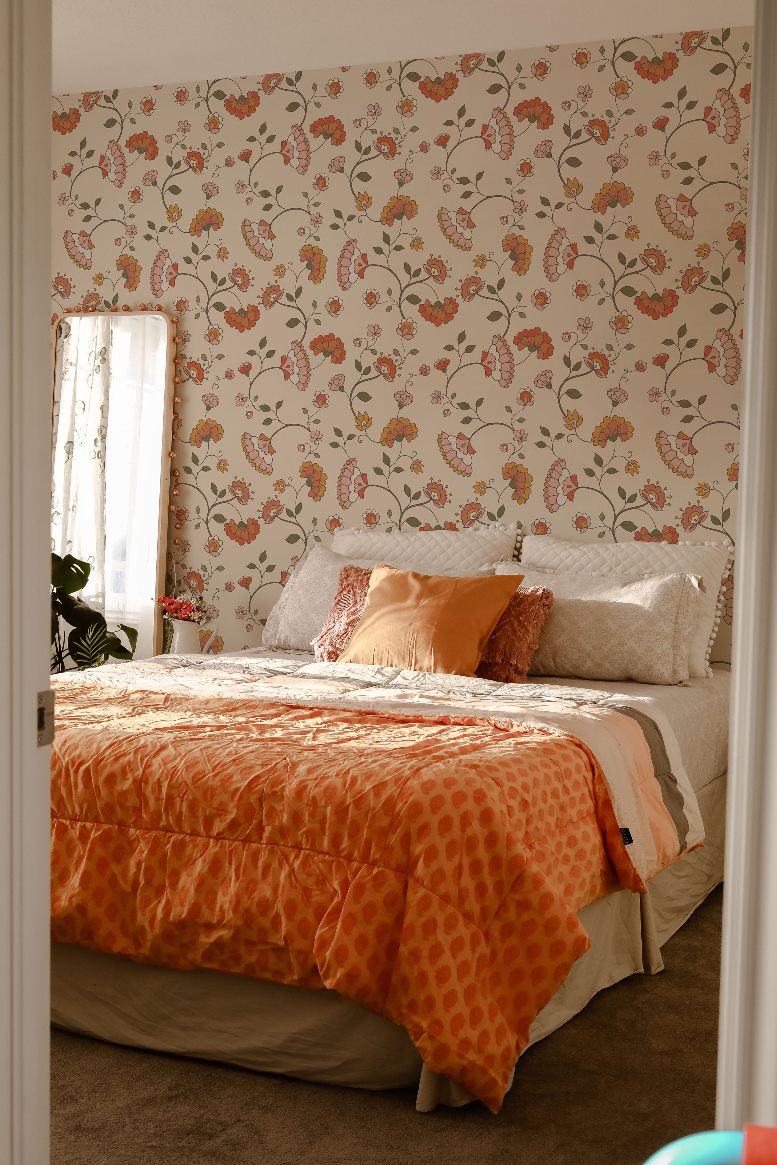 A cozy bedroom filled with natural light, adorned with the Retro Pattern Wallpaper. The room features a bed with an orange textured comforter and decorative pillows in shades of orange and cream, harmoniously blending with the room's warm color scheme