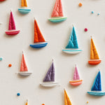 Close-up view of the 'Tidal Sail Wallpaper' showing detailed origami sailboats in various bright colors such as orange, blue, red, and green on a textured cream background, with small colored buttons scattered throughout.