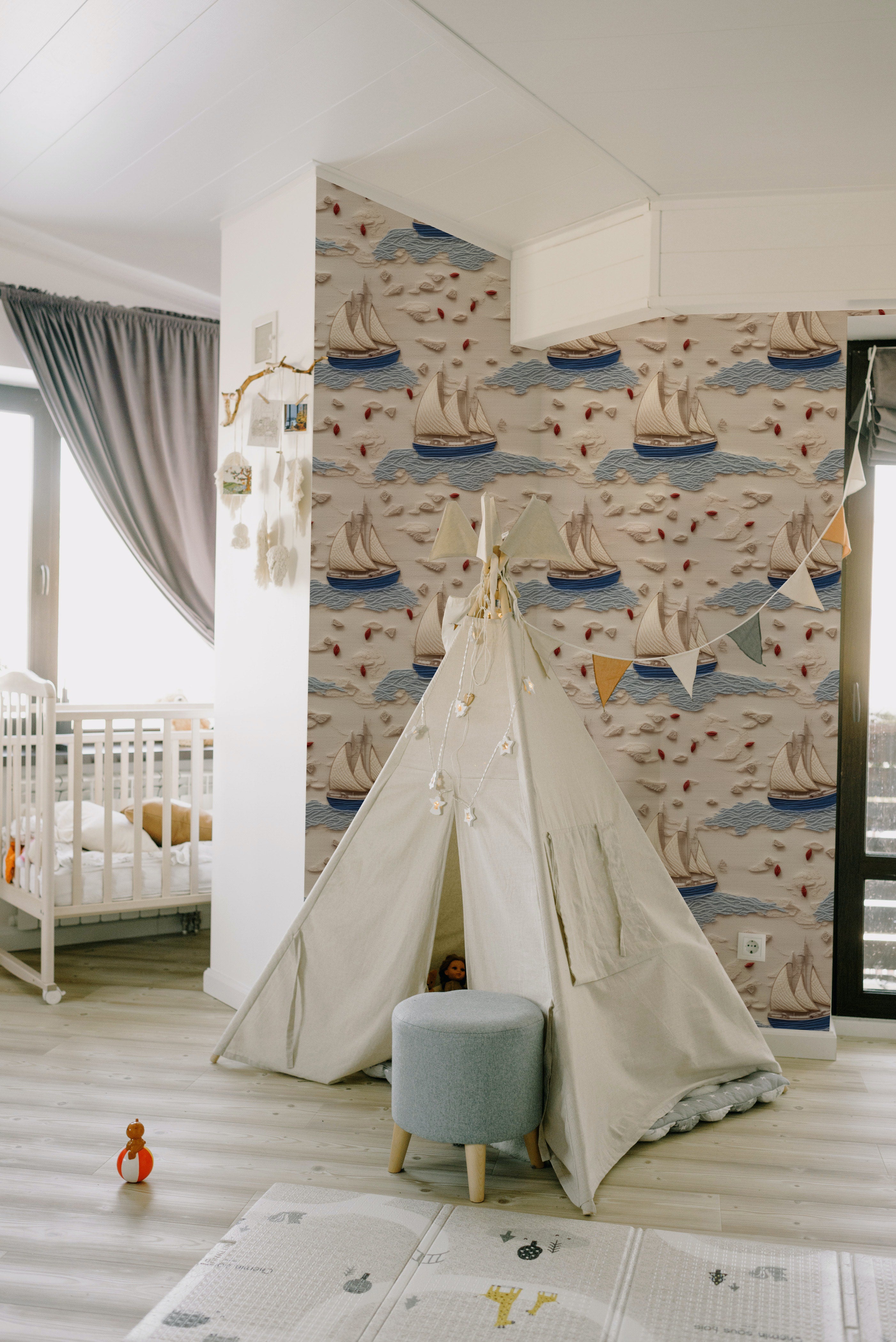 A child's playroom with Coastal Charm Wallpaper, creating a delightful nautical scene with its array of sailboats and gentle waves, complemented by a playful tent and a cozy interior setting.