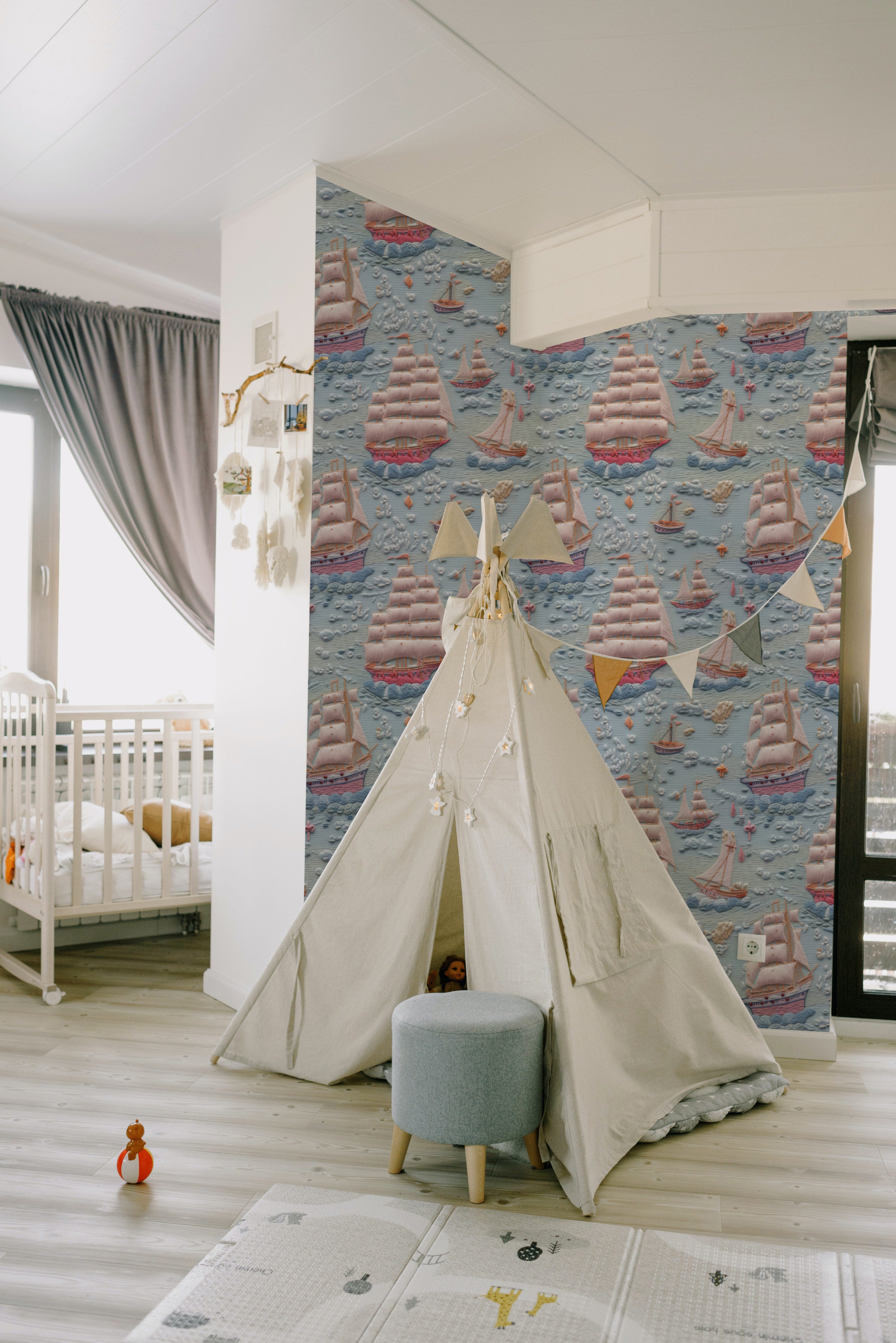 A child's play area with Breezy Sail Wallpaper creating a charming backdrop for a tent and play mat, enhancing the adventurous spirit of the space with its vivid sailboat pattern.