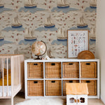 A beautifully decorated nursery room featuring Coastal Charm Wallpaper, which displays an intricate pattern of sailboats on a sandy beige background with soft blue waves and scattered red leaf details, creating a calm, nautical environment.
