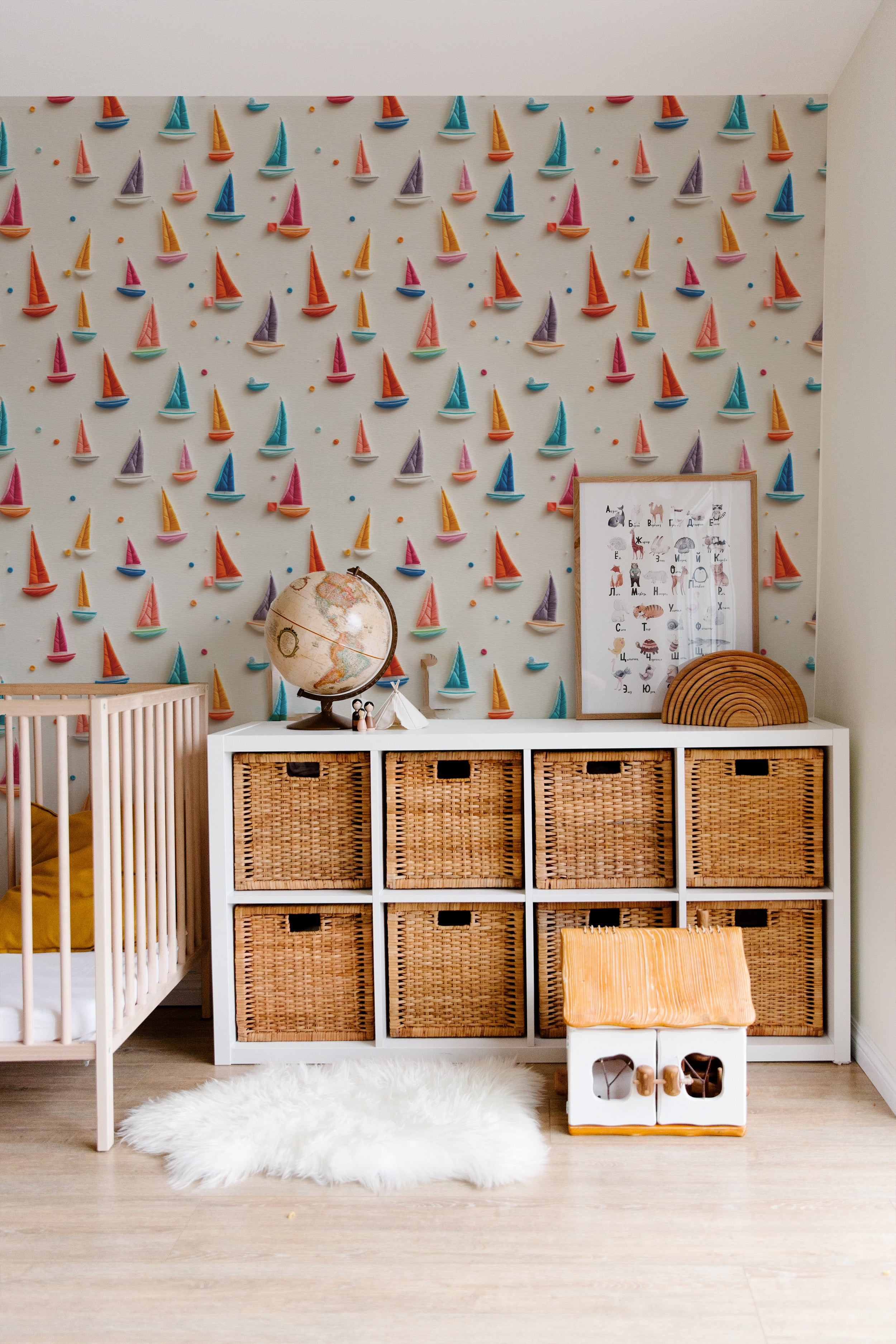 A nursery room with the 'Tidal Sail Wallpaper' enhancing a cheerful and playful environment. The room includes a baby's crib, wooden storage units, and a cozy white fur rug, creating a warm and inviting space.