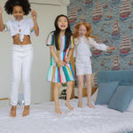 A joyful scene in a children's bedroom with Breezy Sail Wallpaper, where kids are playfully jumping on the bed, surrounded by the lively and colorful sailboat pattern that stimulates imaginative play.