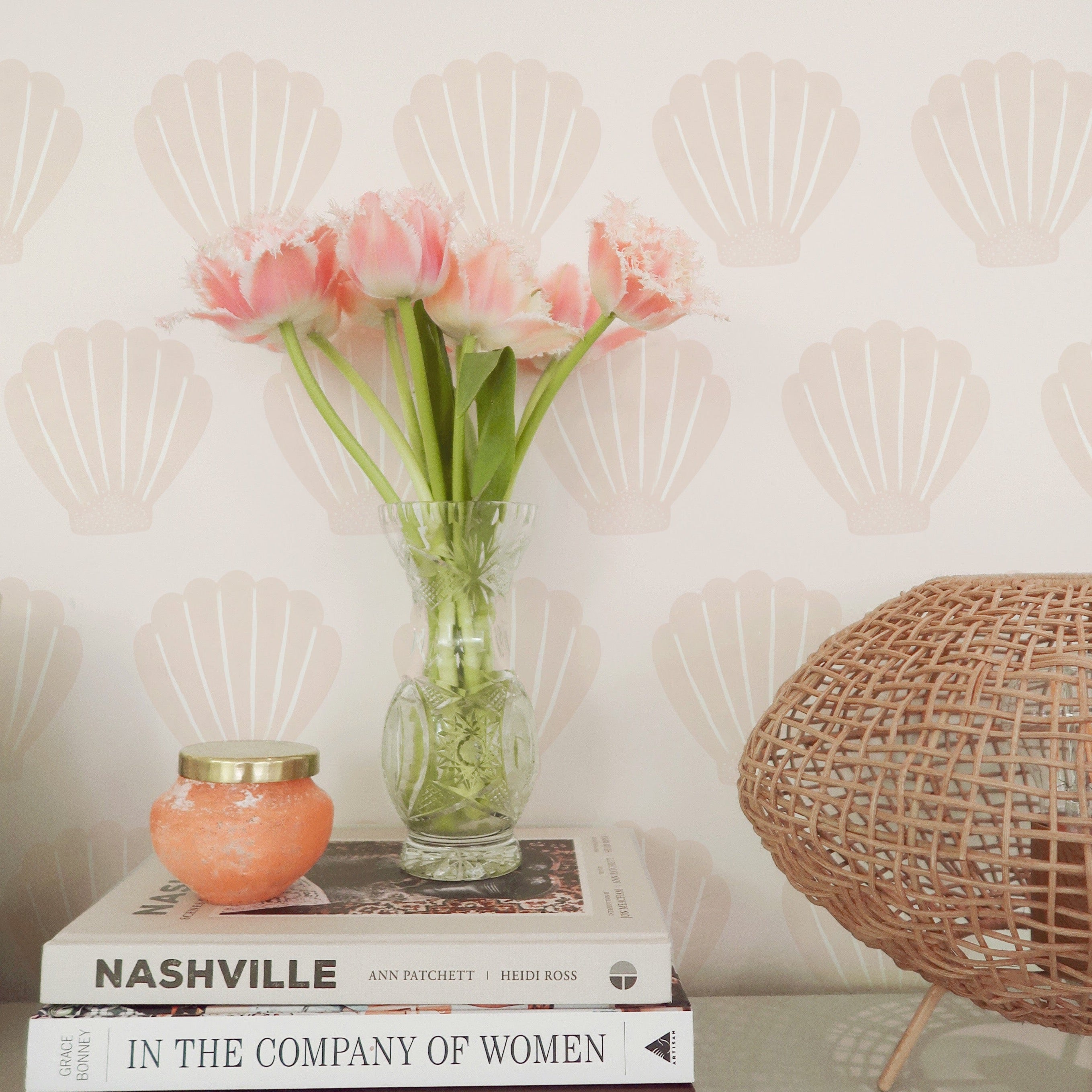 A cozy reading nook with Mermaid Sea Shell wallpaper providing a charming backdrop. The scene includes a wooden chair, a pile of books, and fresh flowers, creating a perfect spot for reading and relaxation.