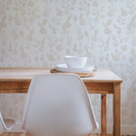 A minimalist dining area with the Cream Watercolour Rose Wallpaper, featuring a simple white chair and a wooden table with a small white bowl and plate set, emphasizing the wallpaper’s role in creating a tranquil dining environment.