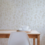A minimalist dining area with the Cream Watercolour Rose Wallpaper, featuring a simple white chair and a wooden table with a small white bowl and plate set, emphasizing the wallpaper’s role in creating a tranquil dining environment.