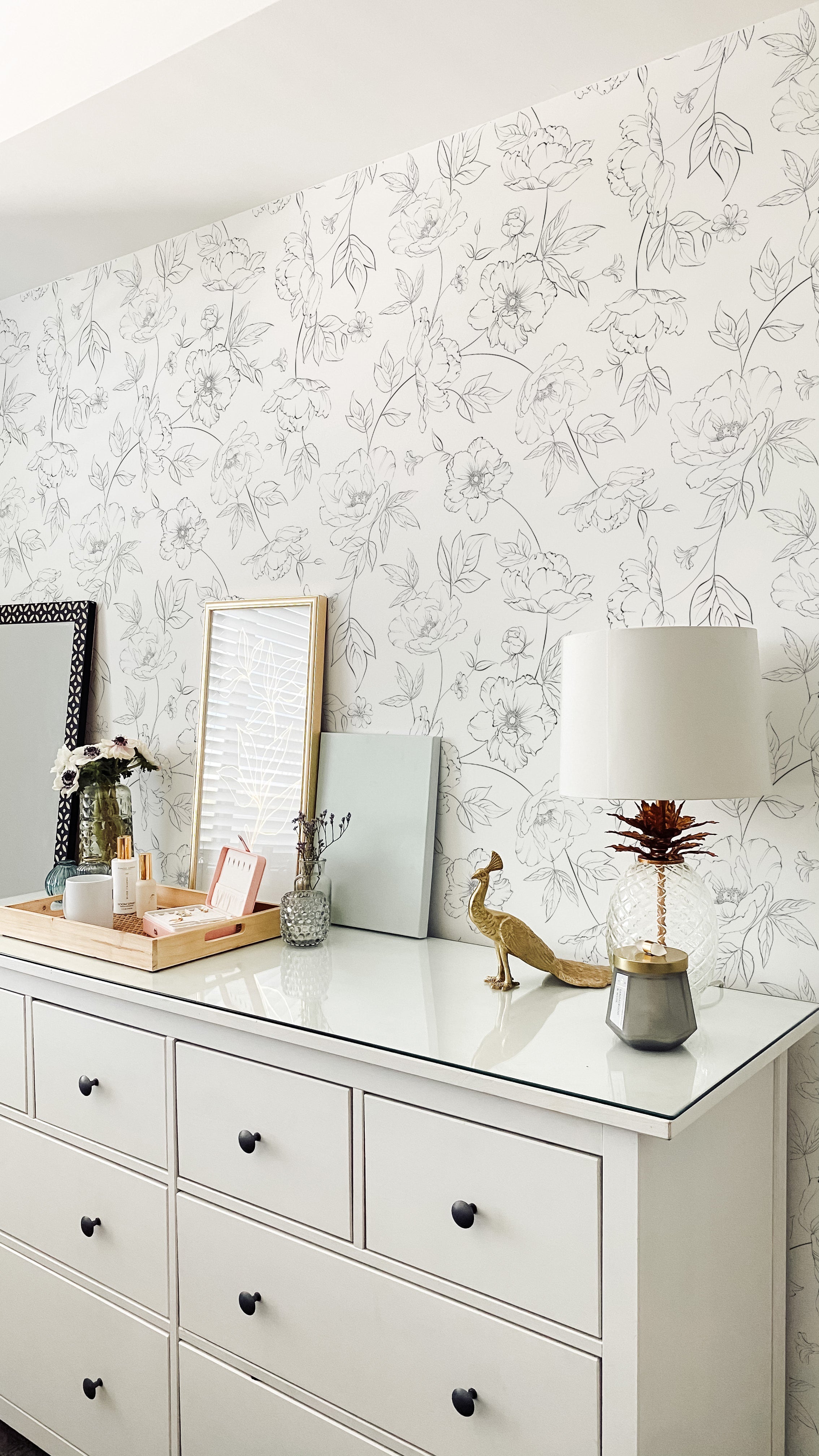 Stylish dresser against Dainty Floral Line Wallpaper, adorned with a variety of modern decorations and a lamp.