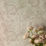  A detailed close-up of the "Woodland Creatures Wallpaper - Beige," showing the intricate sketches of various forest animals and plants. The beige background gives it a soft, warm look that complements the delicate lines and details of the design.