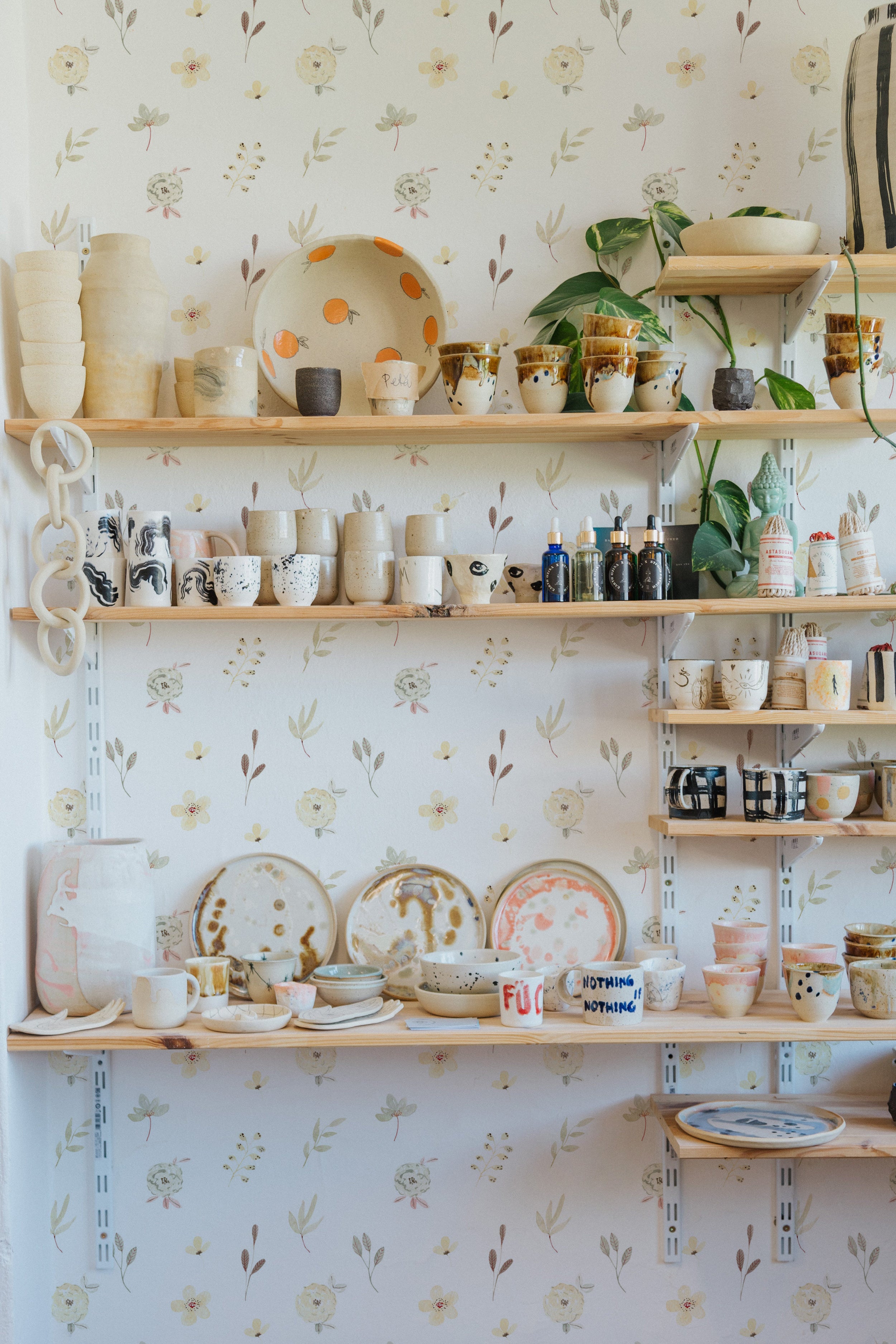 A lively and bright kitchen space with shelves of handcrafted pottery against the Sunny Floral Wallpaper, creating a homey and inviting atmosphere.