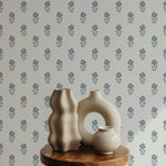 Close-up view of a stylish setup against the Tiny Hydrangea Wallpaper, depicting small blue floral prints on a light gray backdrop. The setting includes abstractly shaped ceramic vases on a wooden stool, emphasizing a modern artistic aesthetic