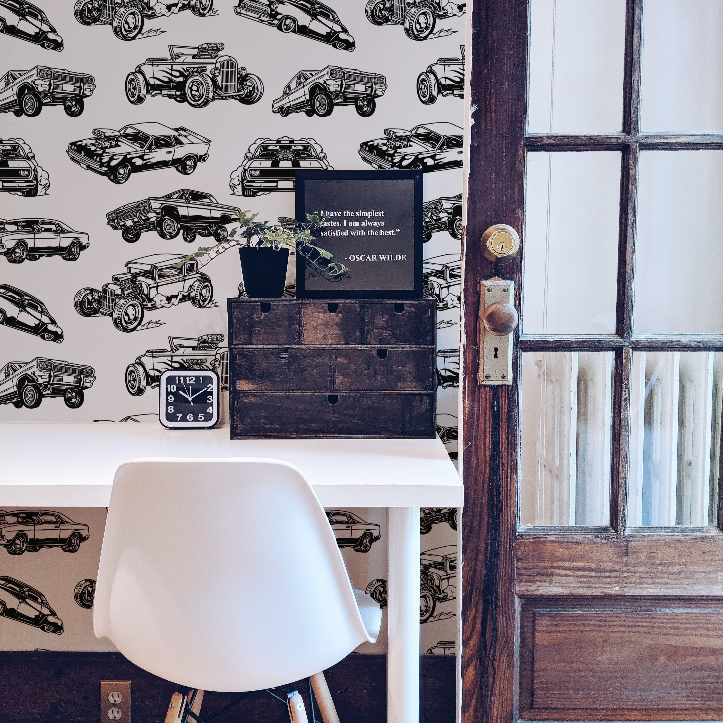 A stylish home office corner featuring Vintage Cars Wallpaper, depicting a variety of classic automobiles in black and white. The workspace includes a white modern chair, a wooden desk with a motivational quote card, enhancing the vintage and sophisticated ambiance.