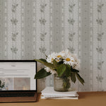 Elegant home office setup featuring Vintage Cutie Wallpaper with olive green floral patterns and ornate vertical stripes on a grey background. The scene includes a stylish workspace with a laptop, a vase of fresh white daisies on books, adding a touch of sophistication