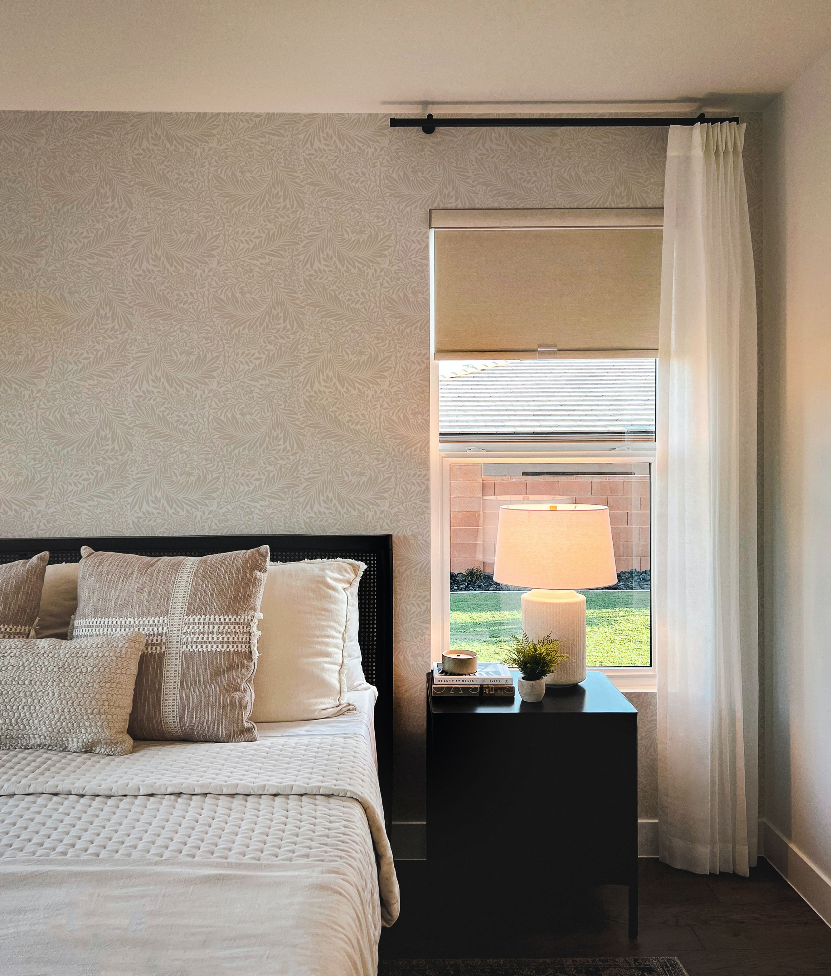 A tranquil bedroom space adorned with 'William Bough Wallpaper' in a botanical print, harmonizing with a neatly dressed bed, side table, and a window with a garden view.