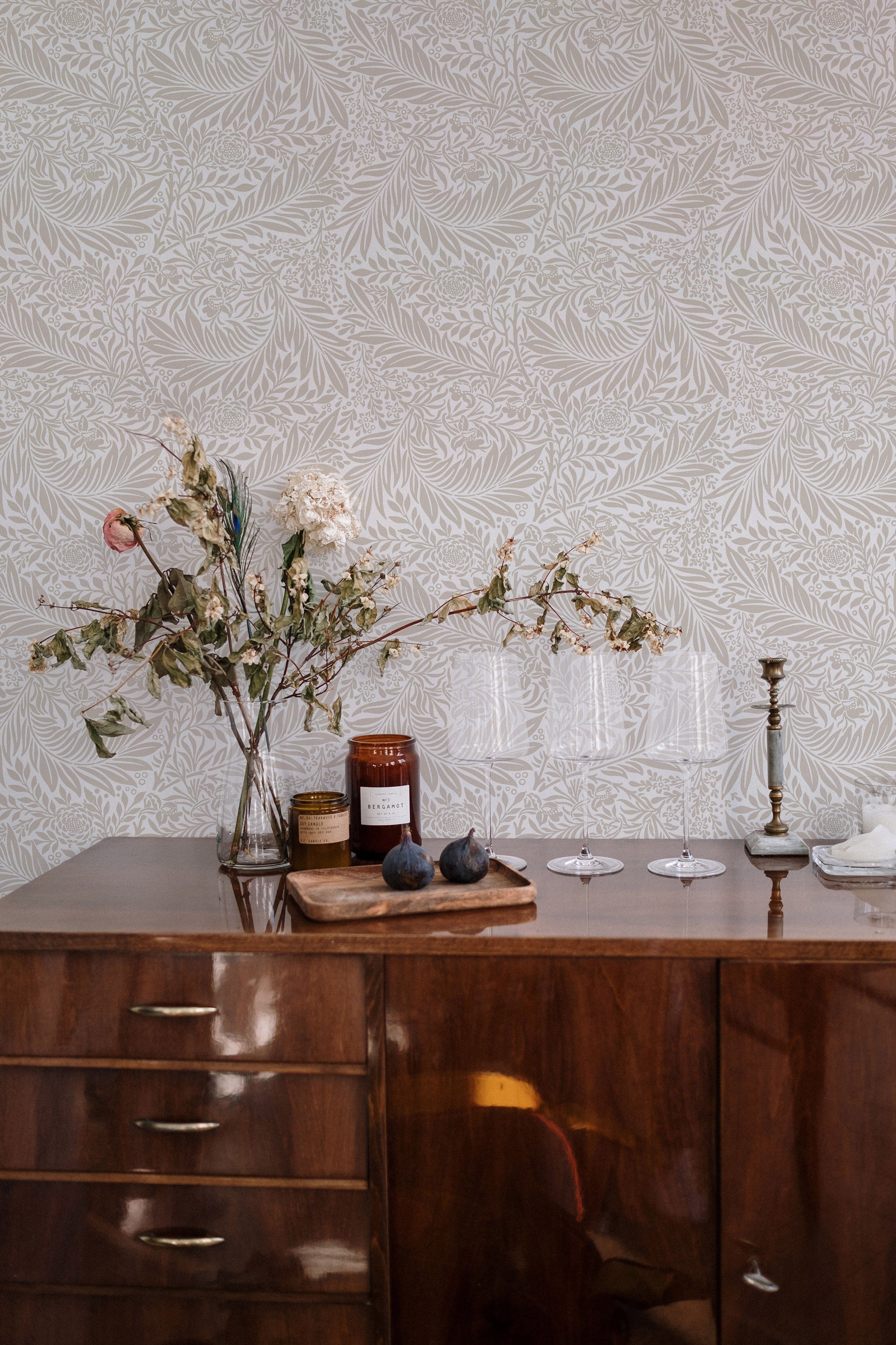 An elegant sideboard against the 'William Bough Wallpaper', decorated with a dried flower arrangement, glassware, and select kitchen items for a rustic-chic look