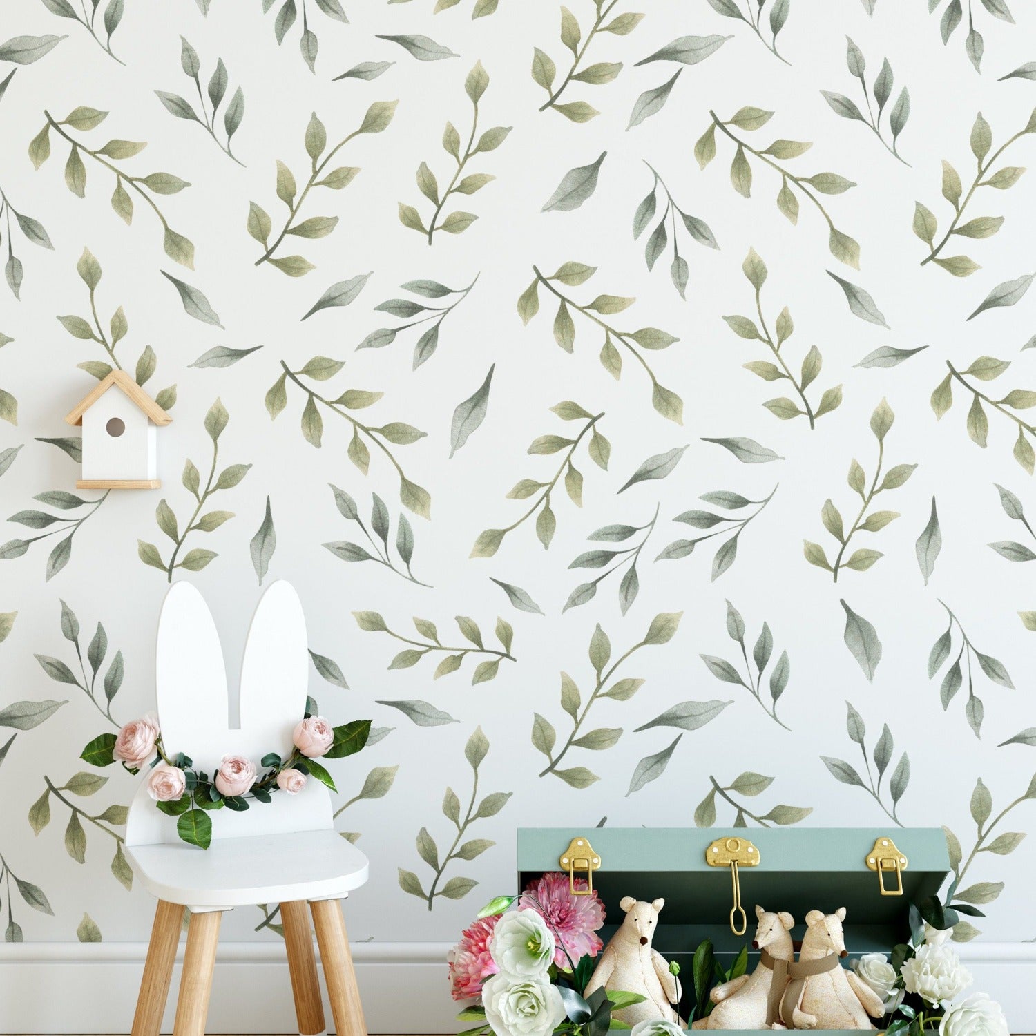 A children's room with one wall decorated with Nursery Green Floral Wallpaper, featuring soft green botanical prints. The natural motif provides a serene backdrop for a white chair adorned with bunny ears and a small shelf with a wooden birdhouse, adding a whimsical touch to the nurturing environment