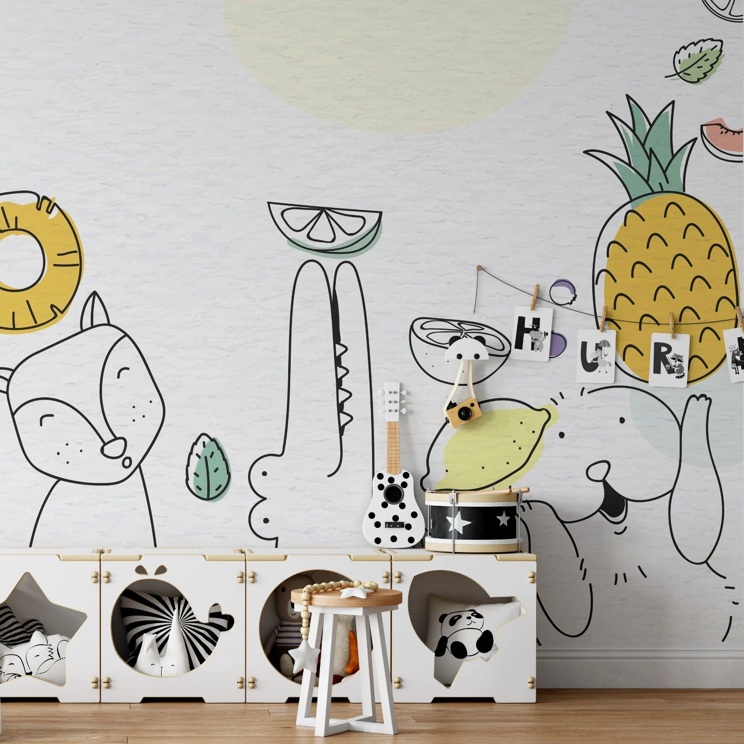 Playful children's room wallpaper featuring whimsical line drawings of various animals and fruits, such as a flamingo, fox, and pineapple, in soft pastel and neutral tones. The illustrations are simple and childlike, with decorative elements like leaves and musical instruments scattered throughout. The wallpaper is complemented by a child-friendly furniture setup including a small wooden stool, toy storage boxes, and a toy train on the floor.
