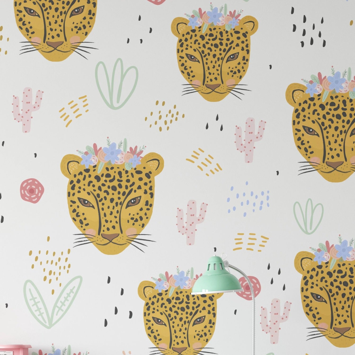 A children's wallpaper design featuring the heads of yellow leopards adorned with flower crowns on a white background. The pattern is interspersed with playful elements like pink cacti, green abstract shapes, and various colorful doodles.