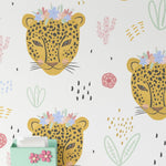 A room decorated with the same children's wallpaper featuring yellow leopard heads with flower crowns. The wallpaper covers the wall behind a white desk with pink and green accessories, creating a lively and cheerful atmosphere.