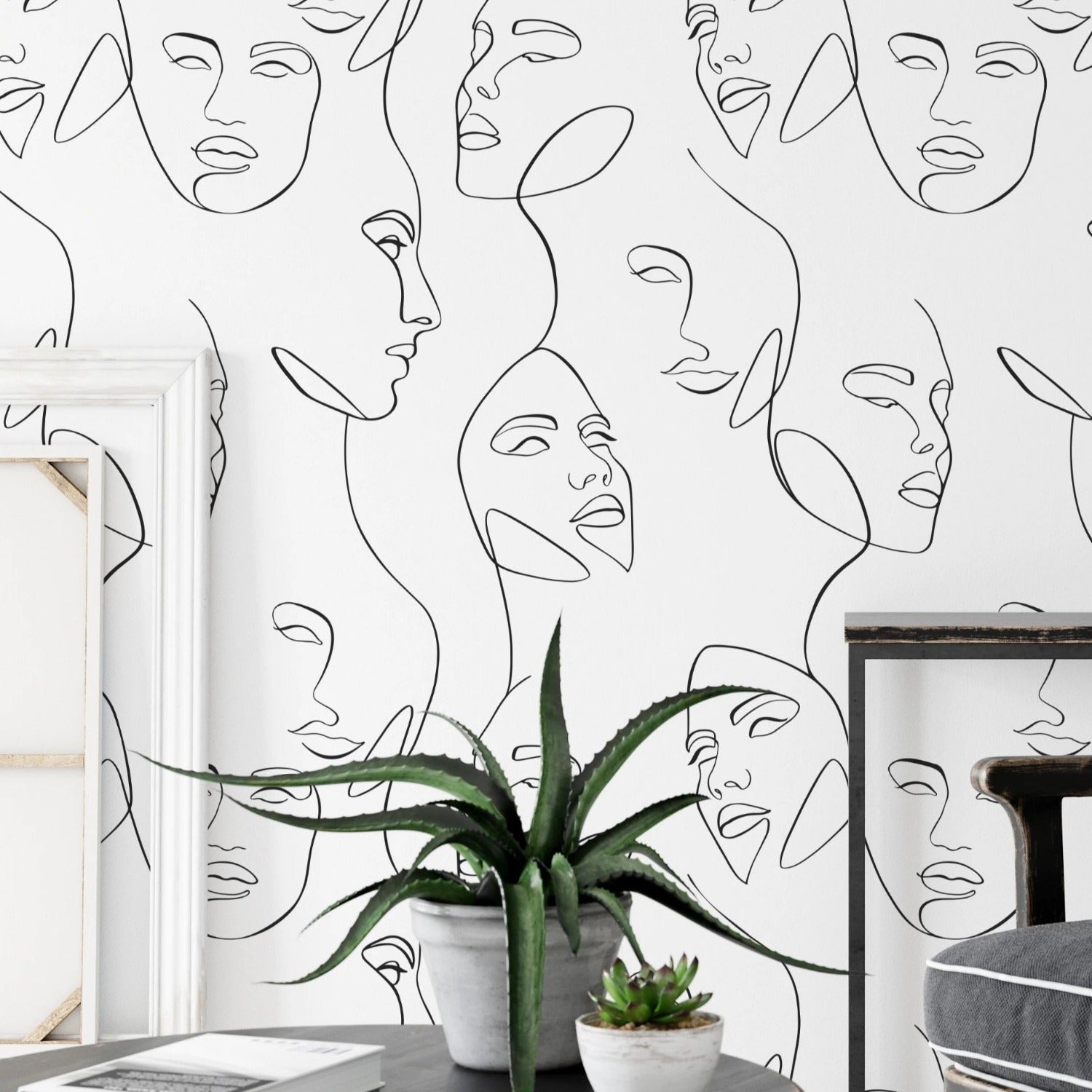 A contemporary room with a wall adorned by the Abstract and Minimal Wallpaper - Line Art III, which displays an array of interconnected black line art faces, offering a bold yet simplistic design element to the space