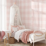 A bright and cozy children's bedroom with a white metal bed and pink bedding against a wall covered in pink plaid wallpaper. The wallpaper features a delicate checkered pattern in soft pink hues, adding a warm and inviting atmosphere to the room. The bed is adorned with pillows and a canopy, creating a dreamy and playful space.