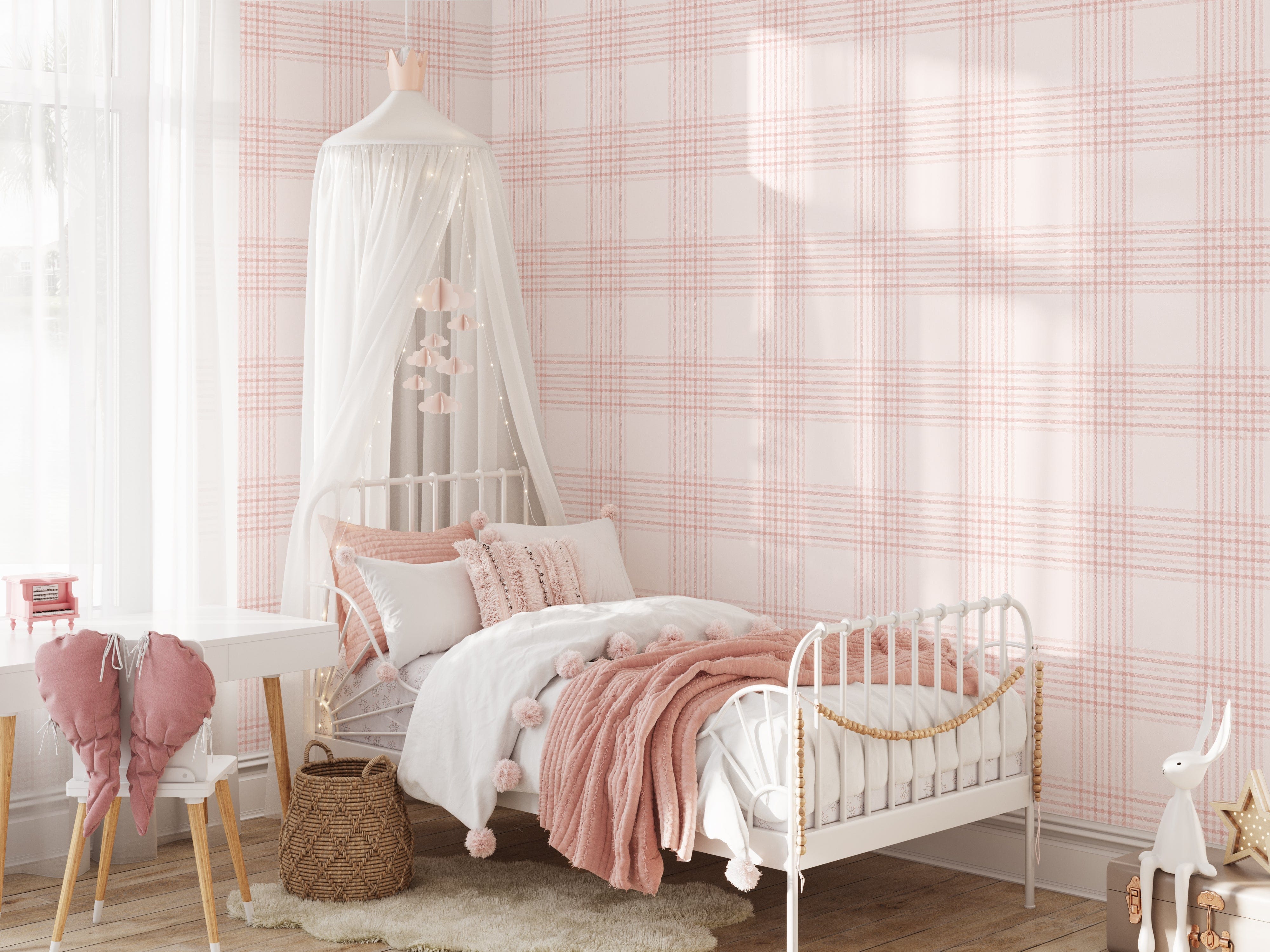 A bright and cozy children's bedroom with a white metal bed and pink bedding against a wall covered in pink plaid wallpaper. The wallpaper features a delicate checkered pattern in soft pink hues, adding a warm and inviting atmosphere to the room. The bed is adorned with pillows and a canopy, creating a dreamy and playful space.