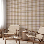 A cozy room with two woven chairs and a small table against a wall covered in black and gold tartan wallpaper. The wallpaper features a classic checkered pattern with intersecting lines of black, gold, and white, adding a touch of bold sophistication to the space. The room is softly lit, enhancing the warm and inviting atmosphere.