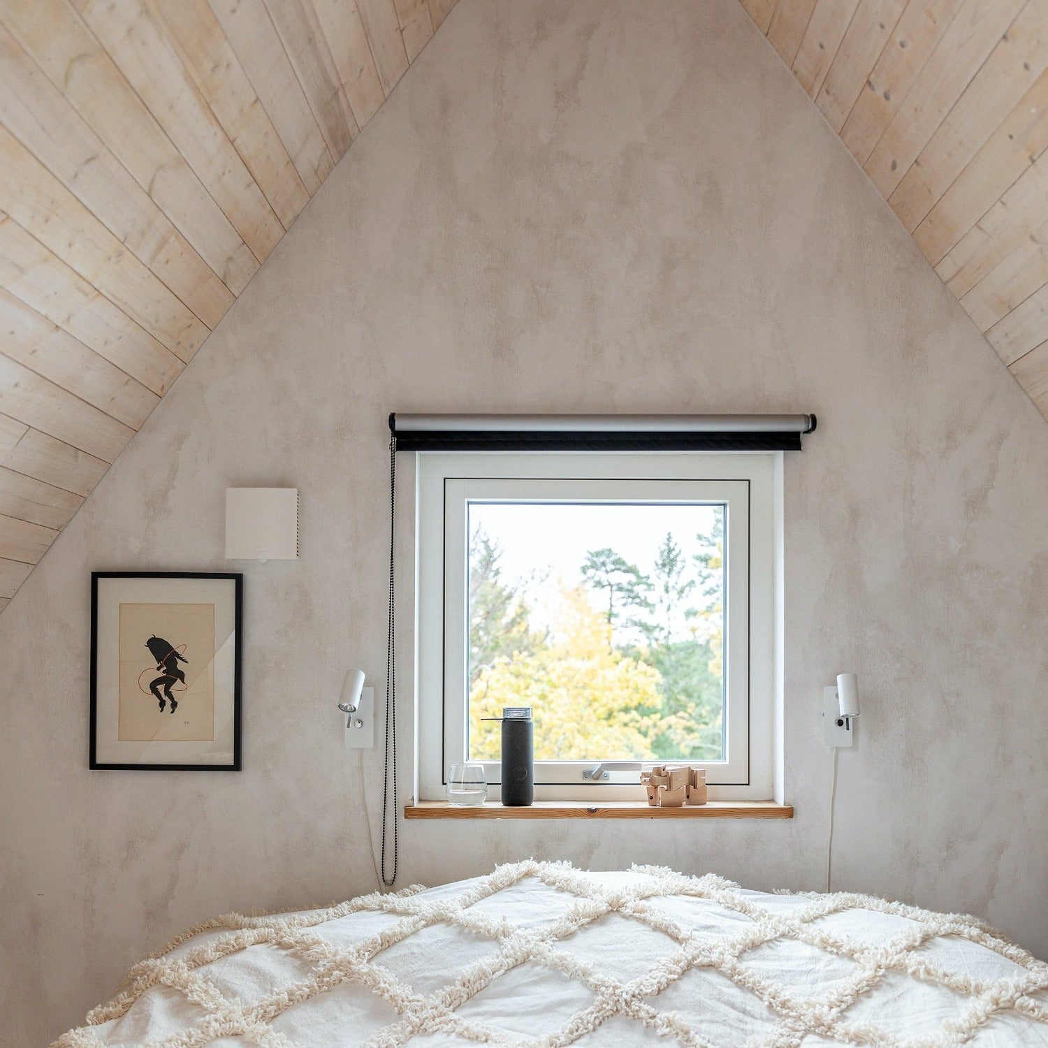 A tranquil attic bedroom adorned with the Neutral Limewash Wallpaper, providing a calming, plaster-like effect that enhances the cozy atmosphere, complemented by a large window inviting in natural light