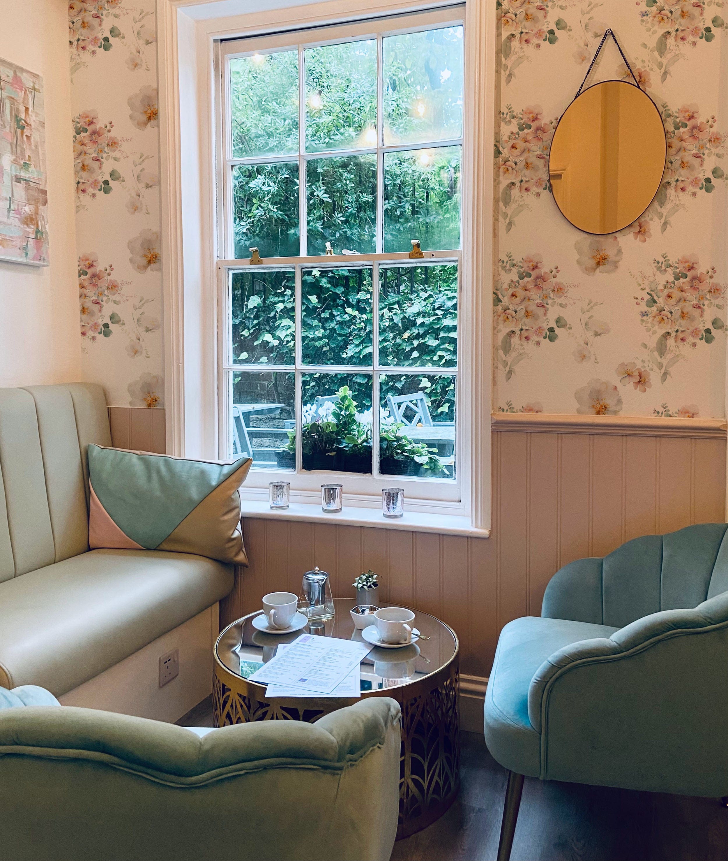 A charming seating area with pastel green chairs and a small round table, complemented by Wild Flora Wallpaper. The floral pattern adds a touch of elegance and tranquility to the room, making it a perfect spot for enjoying a cup of tea and conversation with friends.