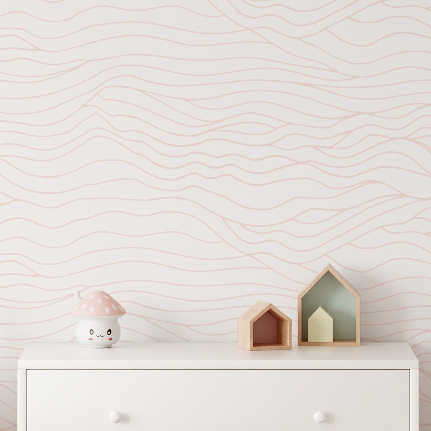 Close-up view of the Line Art Wave Wallpaper in a children's room setting. The wallpaper's delicate wavy lines in pastel pink offer a simple yet playful backdrop, harmonizing with the room's soft color palette and charming décor.