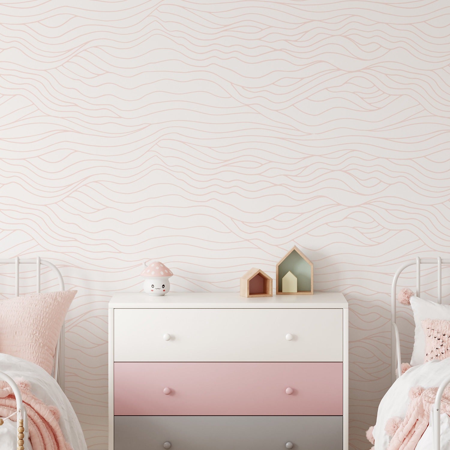 Image of a children's room corner featuring a pastel-hued Line Art Wave Wallpaper with soft wavy lines in a horizontal pattern on a light background. A white and pink dresser sits against the wallpaper with a cute toy mushroom, two small house-shaped shelves, and plush pillows adding to the room's whimsy.