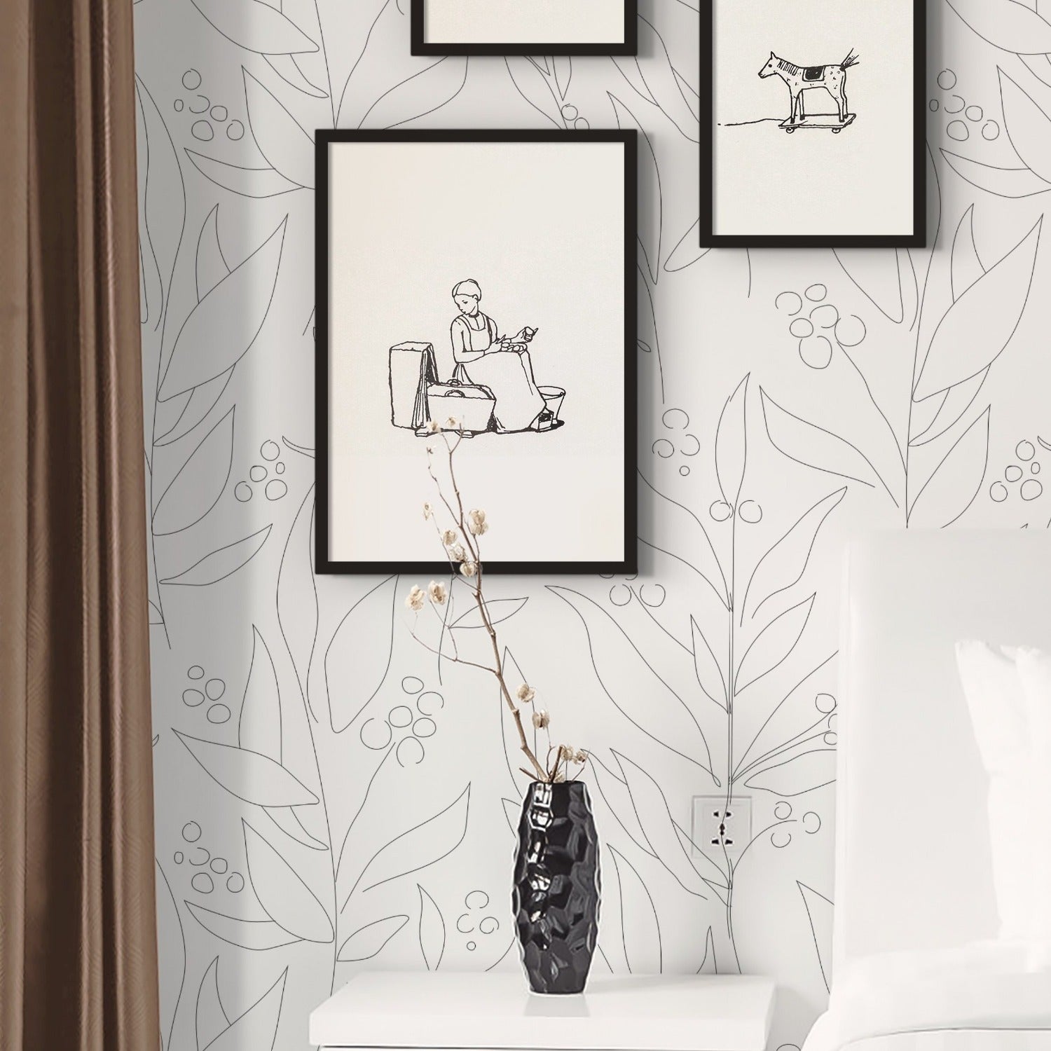 A stylish bedroom featuring a white nightstand, a black vase with flowers, and framed sketches on the wall. The wall is covered with white wallpaper displaying an abstract black floral pattern, creating a serene and modern look.