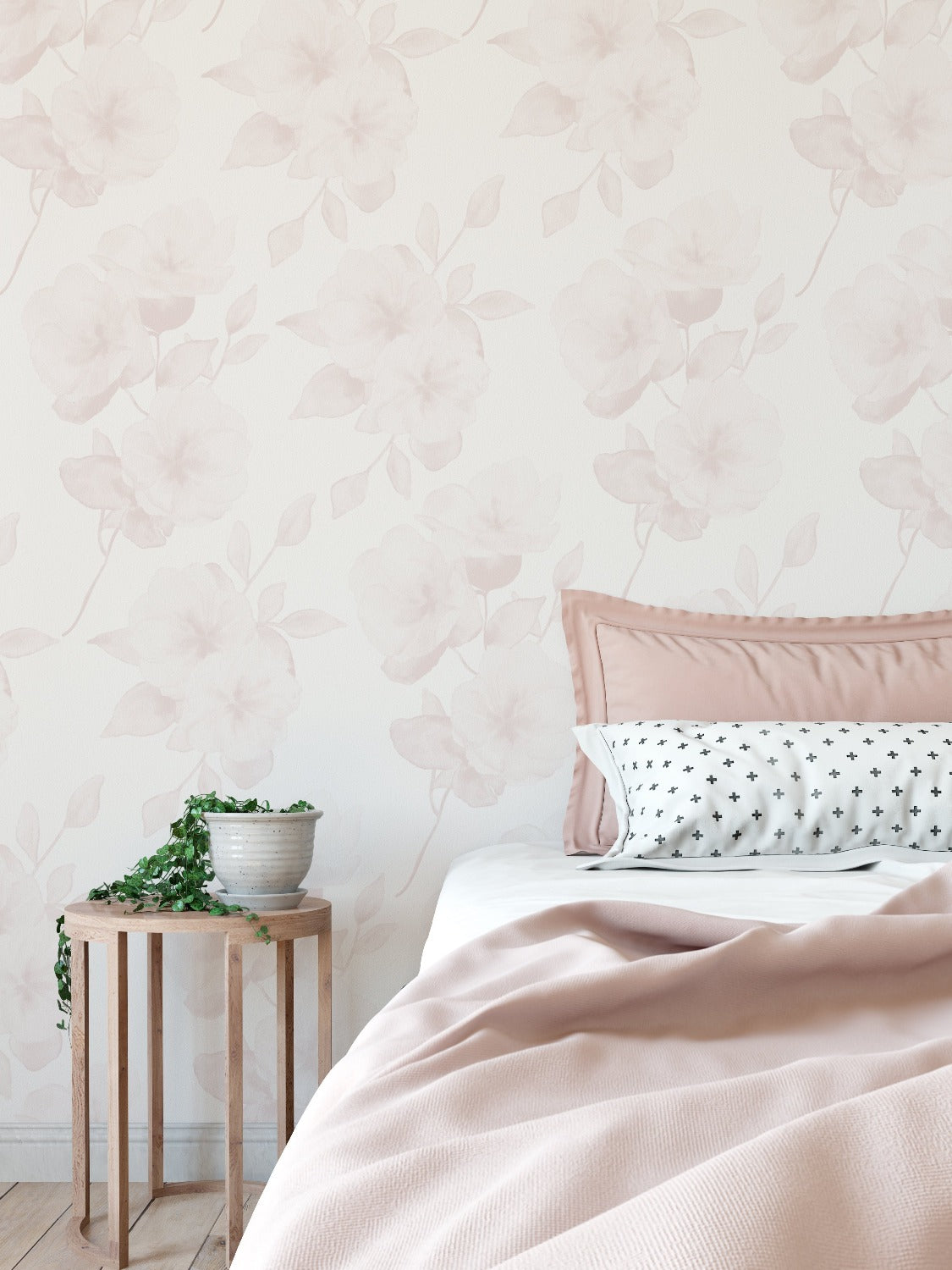 This photo depicts a bedroom interior dressed with the Minimal Floral Wallpaper V on the wall. The wallpaper adds a subtle, elegant touch with its watercolor blush flowers complementing the pastel bedding and wooden bedside table.