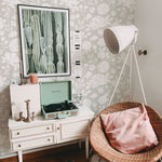 A vintage-styled room corner with 'Silhouette Floral Wallpaper - Silk Green' adorning the wall, complemented by a white vintage dresser, a retro turquoise record player, and a contemporary tripod lamp, blending modern and classic elements.