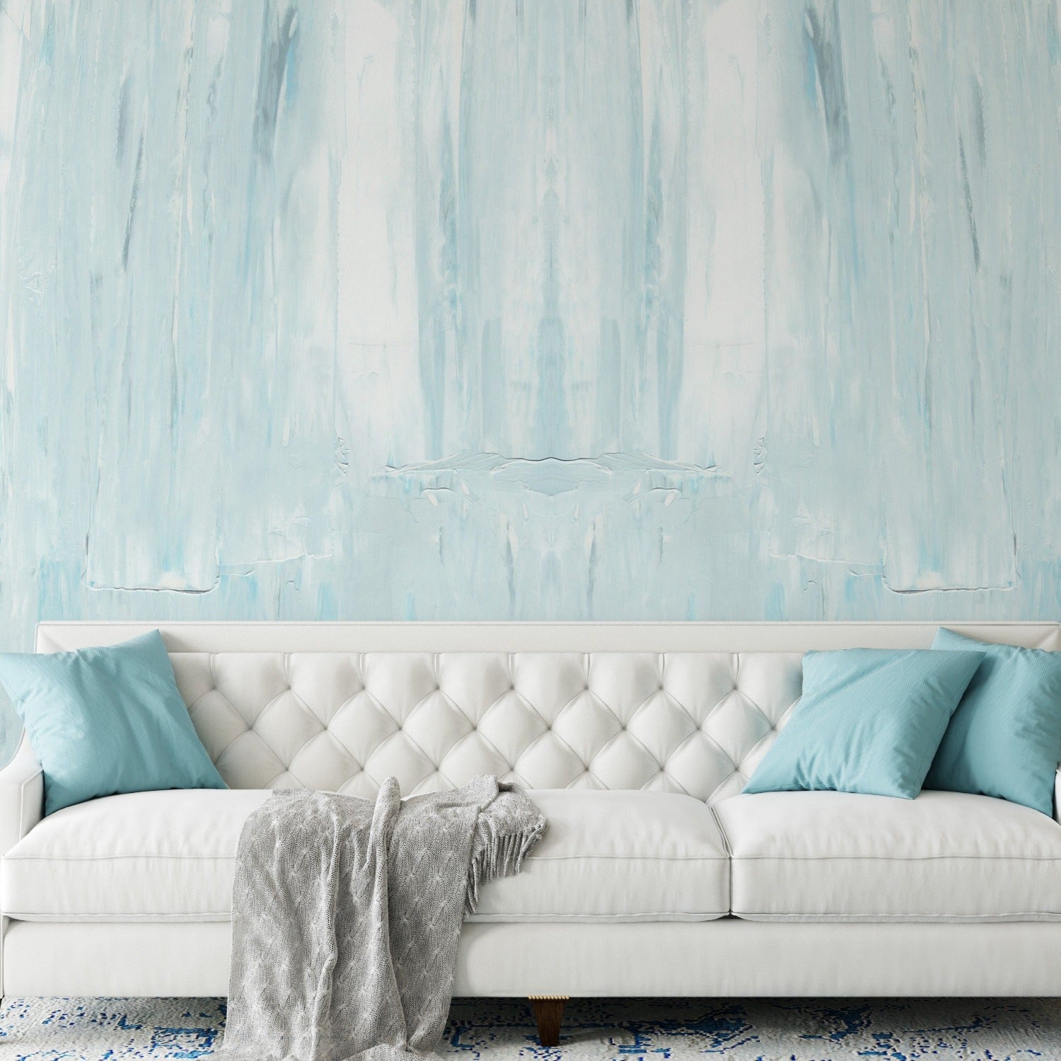 Living room featuring Blue Paint Texture Wallpaper with an abstract, vertical brushstroke design. The wall behind a white tufted sofa with blue throw pillows and a gray blanket showcases the wallpaper's dynamic and artistic texture.