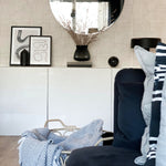An interior room showcasing the Neutral Geometric Wallpaper on one wall, complementing the modern decor with a mirror, vase with dried branches, framed abstract artwork, and a section of a navy blue armchair with a striped throw pillow.