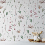A square image featuring Watercolor Floral Wallpaper VII in a domestic setting, with a focus on the detailed pink and mauve flowers and green leaves against an off-white background. The botanical design brings a lively yet gentle ambiance to the room, enhanced by kitchen utensils and natural wood elements in the foreground.