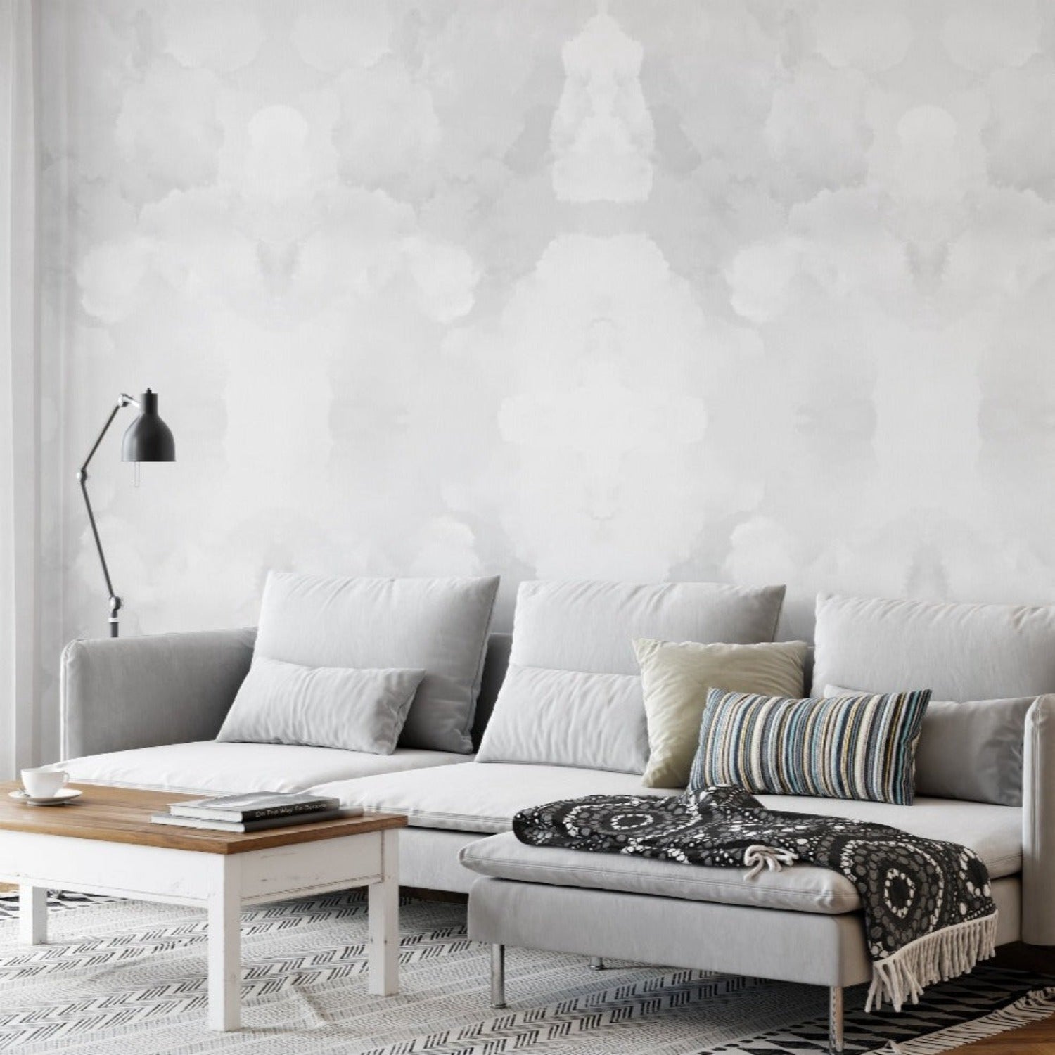 A cozy living room scene showcasing a plush grey sofa against a wall covered in Abstract Grey Wallpaper, featuring a symmetrical pattern of cloud-like grey shapes that provide a soothing backdrop.