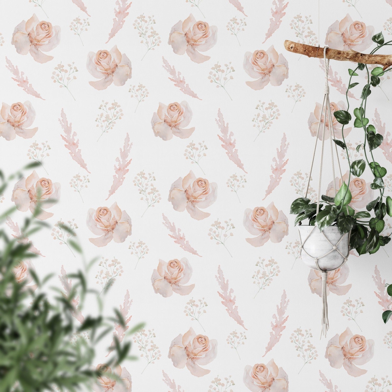 A room decorated with pastel watercolor floral wallpaper. The design showcases peach and pink roses, baby's breath, and light coral leaves on a white background, complementing the greenery of a hanging plant and potted plants in the foreground.