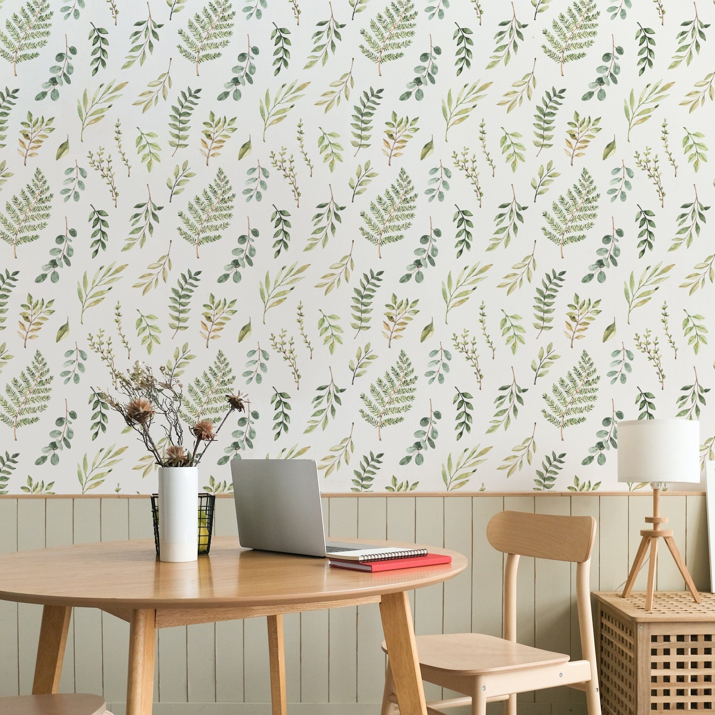 A cozy dining area with a wooden table and chairs, set against a wall decorated with Green Foliage Wallpaper, featuring hand-drawn green leaves and branches on a white background.